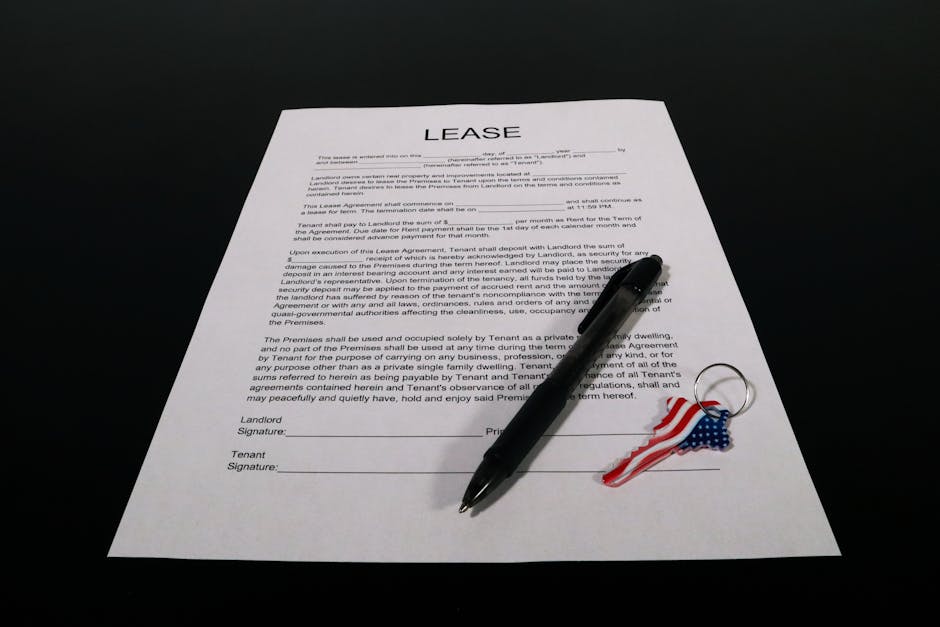 A printed lease agreement document on a black surface, with visible text including the word 'LEASE' at the top. A black ballpoint pen is placed diagonally across the document, and a small decorative k